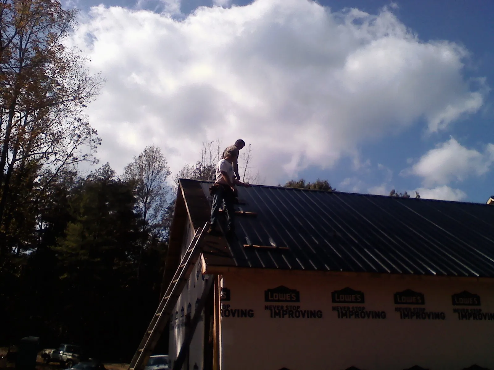 Roofer fastening dark metal panels high against a cloudy sky, from a Roof Inspection job in Manchester